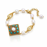 A gold-plated bracelet featuring white baroque pearls, a square gold pendant with turquoise and white pearl details, and leaf-shaped gold links, displayed on a clean white background.
