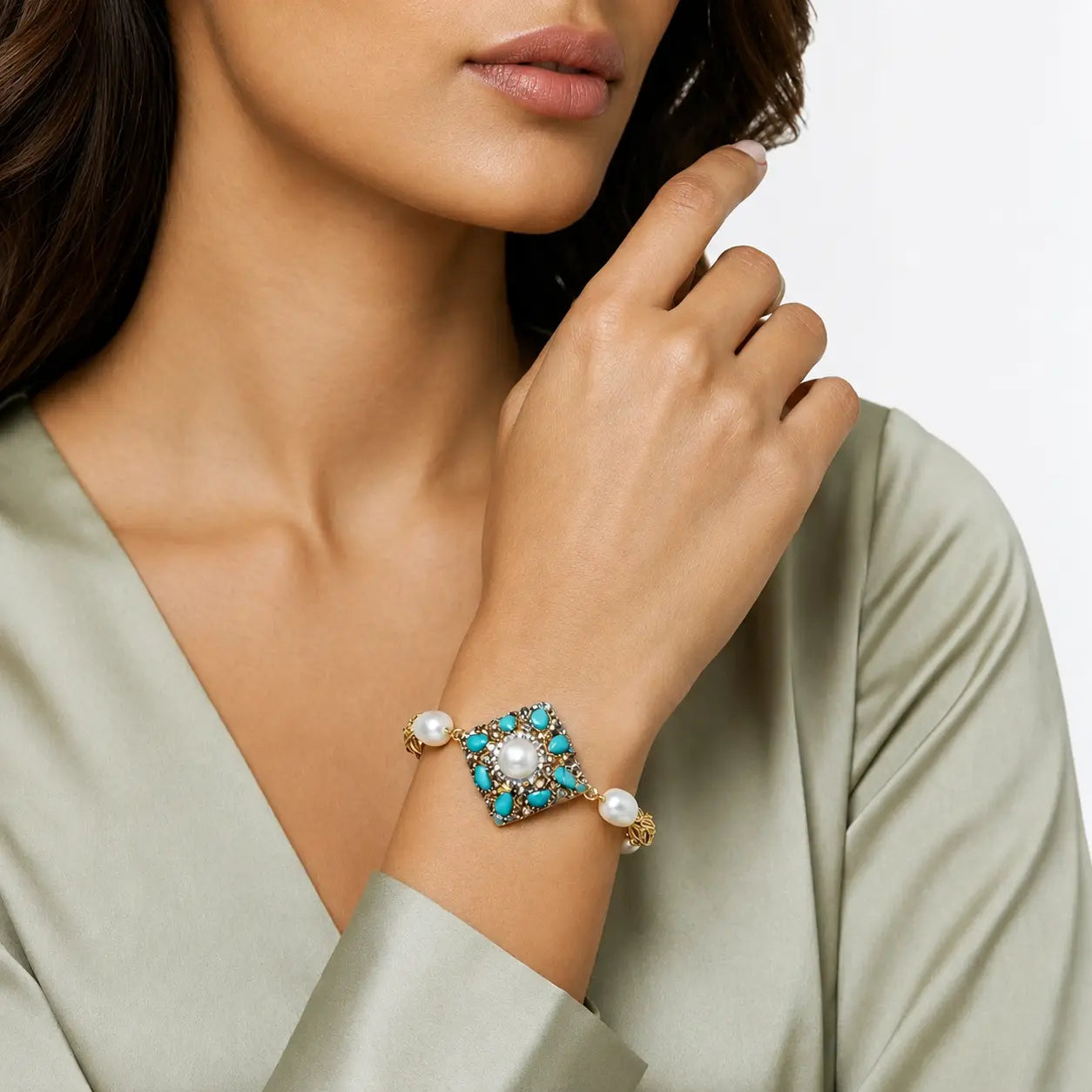 A close-up of a woman wearing a gold-toned cuff bracelet with a turquoise and pearl starburst design, set against a clean white background.