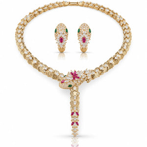 A luxury gold jewelry set featuring a snake-head pendant necklace and matching snake-head earrings, both heavily embellished with clear pavé diamonds and accented with green emerald-cut gemstones and pink ruby-cut gemstones, displayed on a clean white background.