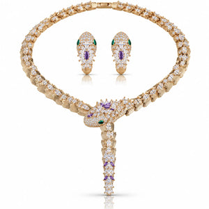 A gold jewelry set featuring a snake pendant necklace and matching snake earrings, embellished with clear pavé diamonds and accented with green and purple gemstones, shown on a white background.