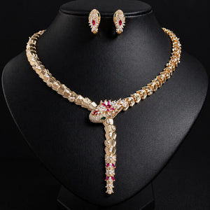 Gold-plated snake necklace and matching stud earrings displayed on a black jewelry bust. The necklace and earrings are adorned with clear rhinestones and accented with small red and green gemstones at the head of the snake.