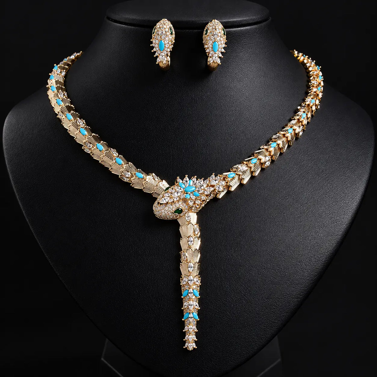 Gold-plated statement necklace and matching stud earrings set with turquoise blue and clear rhinestones, displayed on a black jewelry bust.