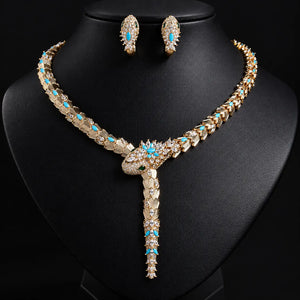 Gold-plated statement necklace and matching stud earrings set with turquoise blue and clear rhinestones, displayed on a black jewelry bust.