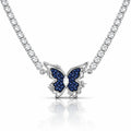 A silver-tone butterfly pendant necklace featuring dark blue pavé-set wings and a clear central stone, suspended from a sparkling silver chain on a white background with a soft reflection.