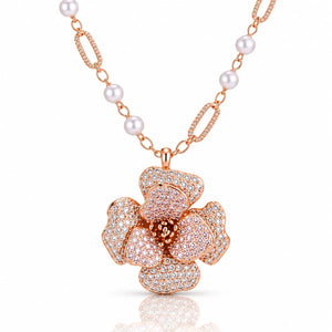 Rose gold floral pendant necklace with a flower-shaped centerpiece paved with clear stones and a chain featuring white pearls and textured rose gold links, shown on a white background with a soft reflection.