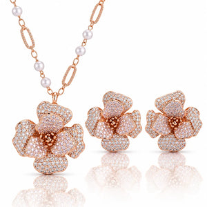 Rose gold jewelry set featuring a flower-shaped pendant necklace, matching stud earrings, and a chain with white pearls on a clean white background with reflections.