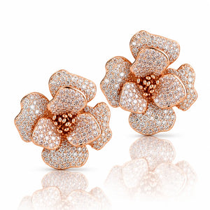 A pair of rose gold flower-shaped stud earrings paved with small clear stones, shown on a clean white background with a soft reflection below.