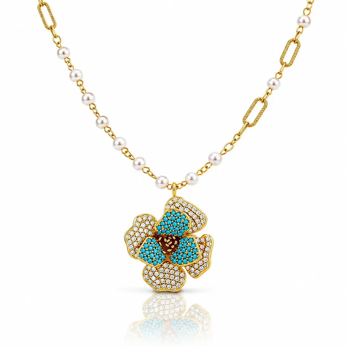 A gold chain necklace featuring white pearls and a gold pendant shaped like a flower, embellished with turquoise blue stones and small clear pavé stones, shown on a white background with a soft reflection.