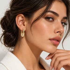 A close-up of a woman wearing a delicate gold huggie hoop earring adorned with small clear crystals, set against a clean, light background.