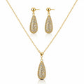 Gold jewelry set featuring a teardrop-shaped pendant necklace and matching drop earrings, both adorned with pavé-set clear stones on a white background.