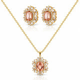 Gold jewelry set featuring a pendant necklace and matching stud earrings with oval peach-pink center stones surrounded by clear crystals on a white background.