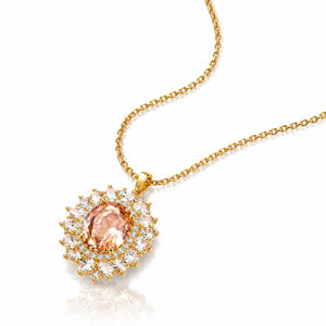 A gold chain necklace with a sunburst pendant featuring a central peach-colored gemstone surrounded by clear accent stones, shown on a white background with a soft reflection.