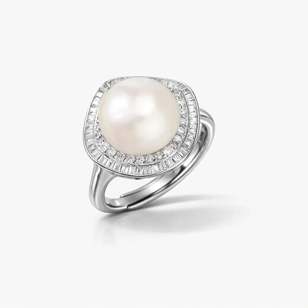 Silver ring with large round pearl center and halo of small clear gemstones on white background