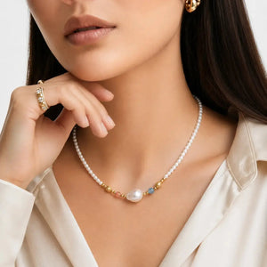 A close-up lifestyle shot of a model wearing a delicate pearl necklace with gold and colorful spacer beads, along with matching gold jewelry.