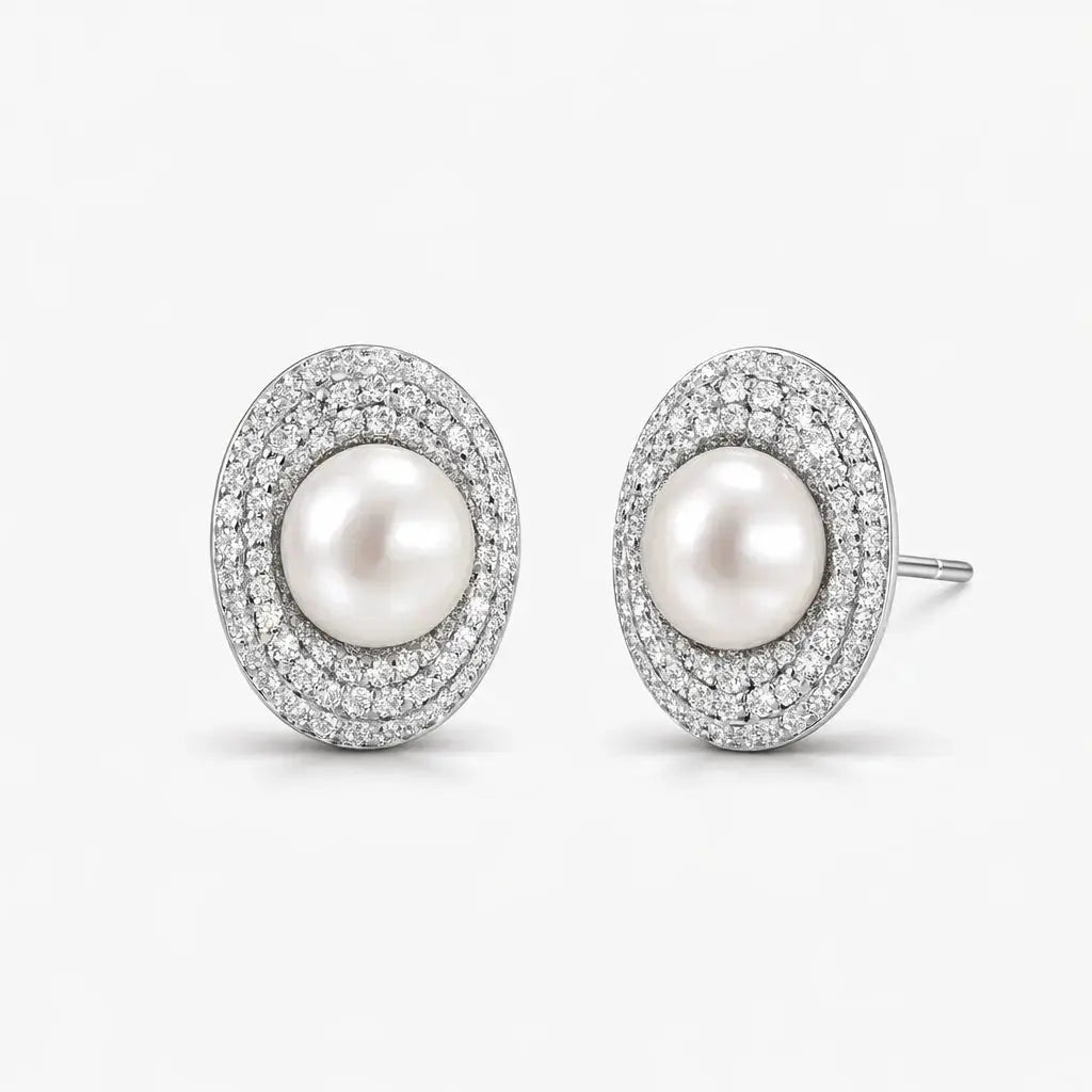 Elegant oval pearl stud earrings with double halo of sparkling pave stones on white background.