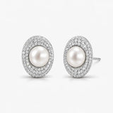 Elegant oval pearl stud earrings with double halo of sparkling pave stones on white background.