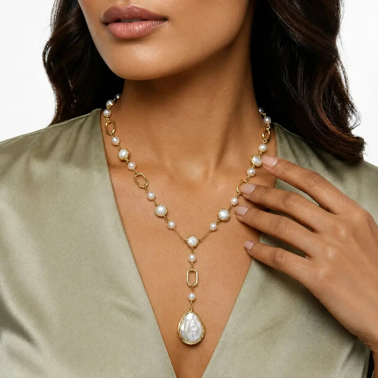 A close-up of a woman wearing a gold and pearl necklace with a large teardrop pearl pendant, paired with an olive green satin top.