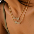 Close-up of a person wearing two layered gold necklaces with script name pendants, one reading 'Deblah' and the other 'Athena', set with small clear stones.
