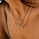 Close-up of a person wearing two layered gold necklaces with script name pendants, one reading 'Deblah' and the other 'Athena', set with small clear stones.