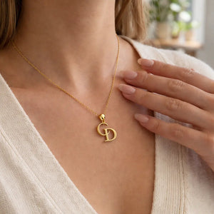 Gold necklace with a pendant worn by a person, with a blurred indoor background.