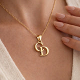 A close-up of a gold chain necklace with a monogram pendant featuring the letters 'G' and 'D', worn on a model's neck with a hand resting near the jewelry.