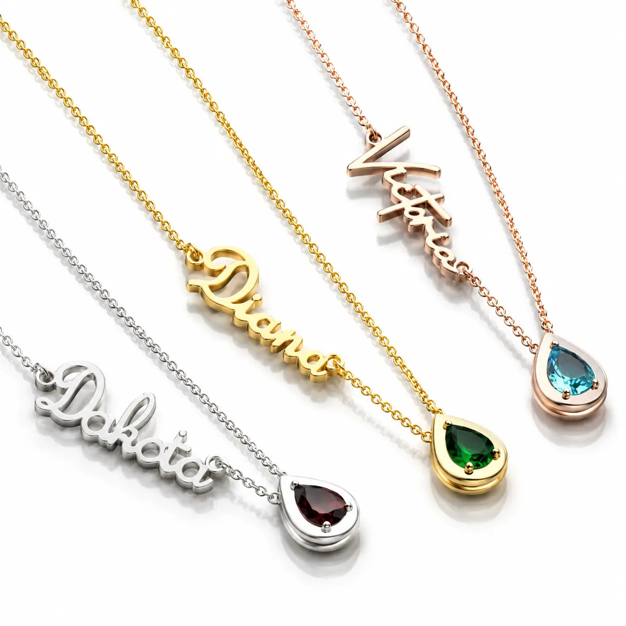 Four personalized name necklaces with teardrop gemstone pendants displayed diagonally on a white background. The necklaces are made of gold, rose gold, and silver metals and feature the names Diana, Victoria, Dakota, and Doria with teardrop-shaped gemstones in green, blue, burgundy, and rose gold.