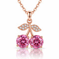 Rose gold cherry pendant necklace featuring two round pink gemstones in the shape of cherries, with leaf details paved with small clear stones, shown on a white background with a reflection.