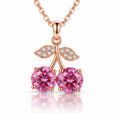 Rose gold cherry pendant necklace featuring two round pink gemstones in the shape of cherries, with leaf details paved with small clear stones, shown on a white background with a reflection.