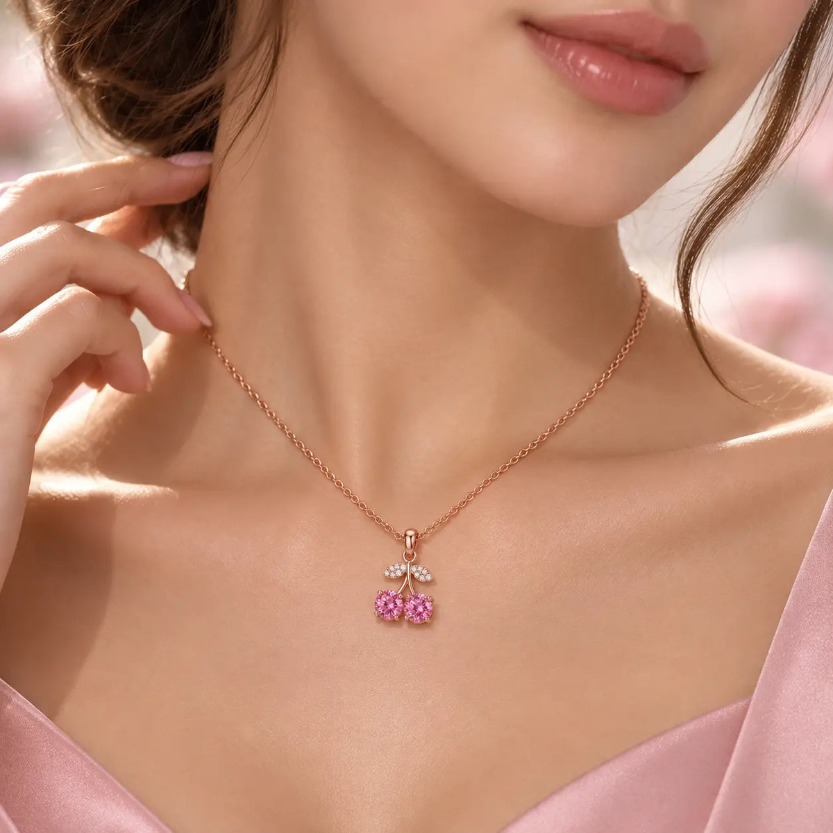 Rose gold cherry pendant necklace featuring two round pink gemstones in the shape of cherries, with leaf details paved with small clear stones, shown on a white background with a reflection.