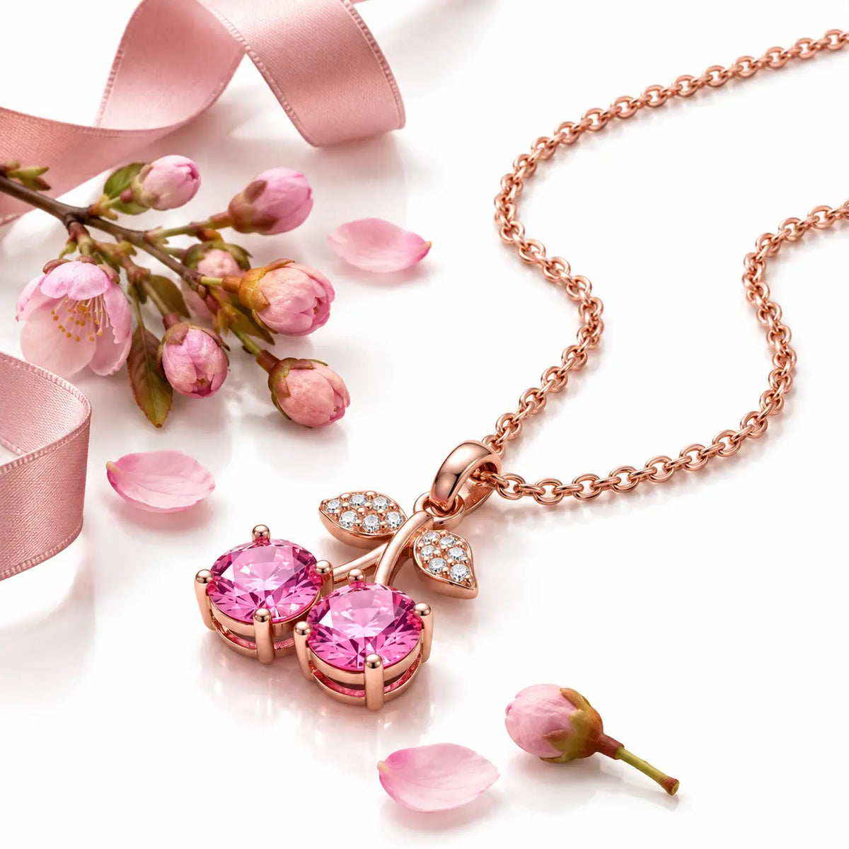 Rose gold cherry pendant necklace featuring two round pink gemstones in the shape of cherries, with leaf details paved with small clear stones, shown on a white background with a reflection.