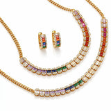 Gold jewelry set featuring a necklace, matching earrings, and a bracelet, each adorned with baguette-cut rainbow-colored stones and clear pavé accents on a white background.