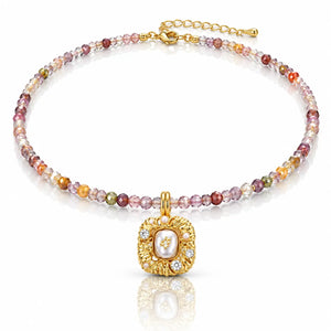 A gold beaded necklace with a central pendant featuring a white pearl surrounded by small clear stones, accented with multicolored faceted beads in pink, orange, yellow, and green tones, set against a clean white background with a soft reflection.