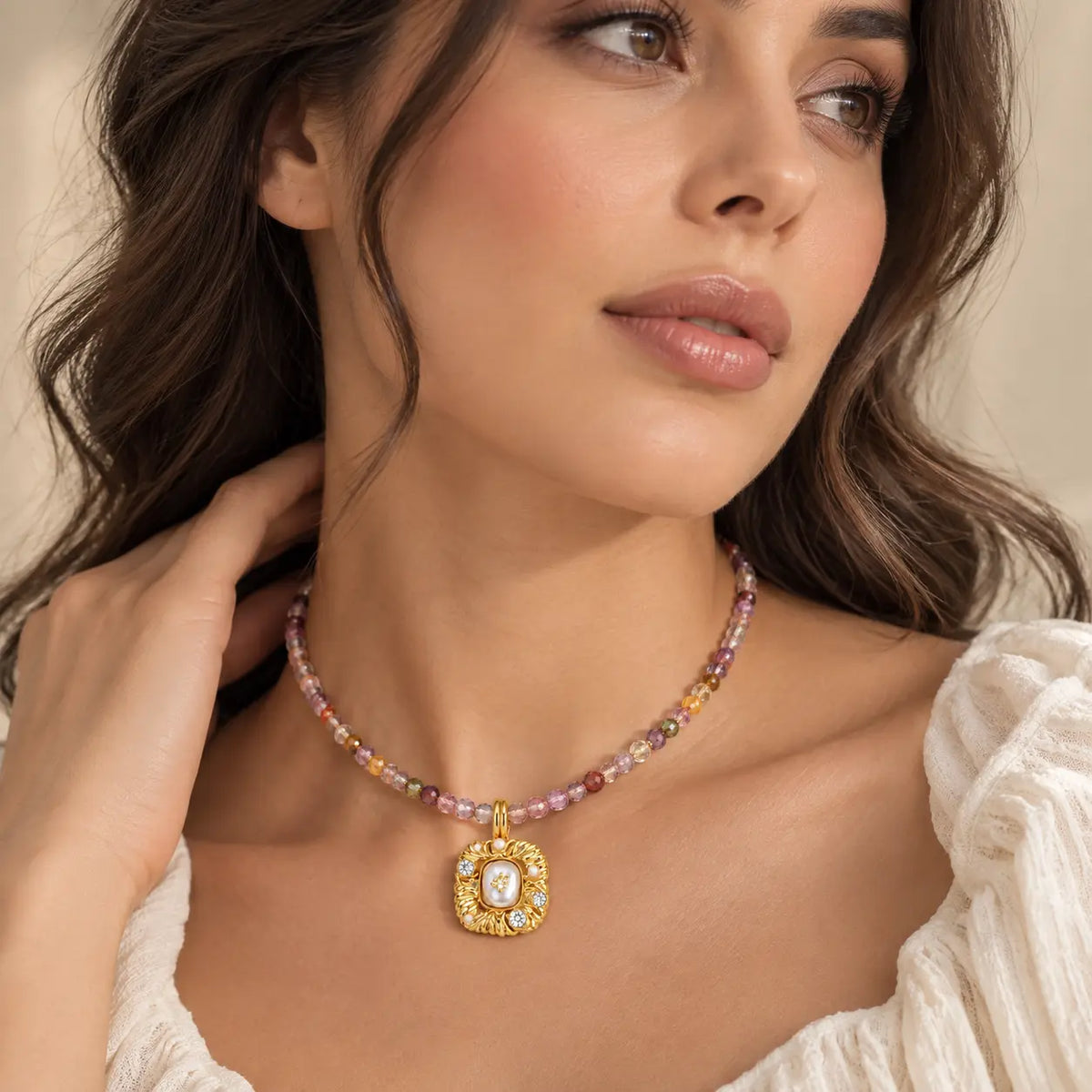 A close-up of a woman wearing a delicate beaded necklace with a gold pendant. The necklace features small, multicolored beads in shades of pink, purple, and gold, with a central gold medallion pendant containing a white stone.