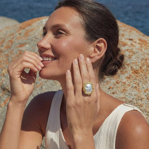 Woman wearing a large ring on a rocky beach with water in the background