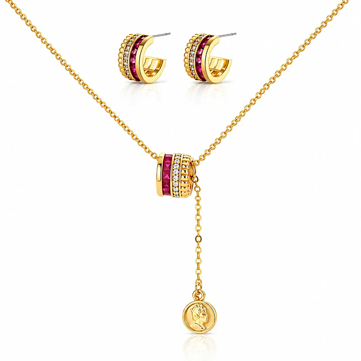 Gold jewelry set featuring a necklace with a cylindrical charm flanked by red gemstones and clear stones, matching hoop earrings, and a round pendant with an embossed profile, displayed on a white background.