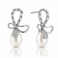 A pair of silver drop earrings featuring a bow-shaped top set with baguette and round clear stones, a teardrop-shaped clear stone pavé setting, and a large white pearl dangling below, shown on a white background with a soft reflection.