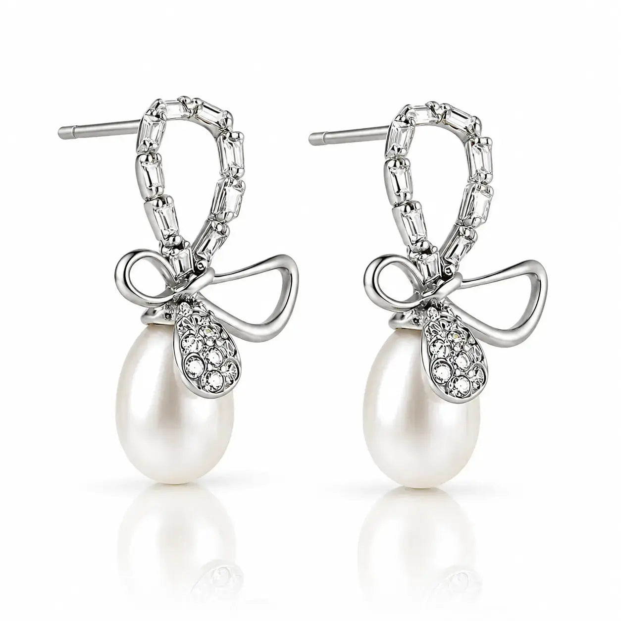 A pair of silver drop earrings featuring a bow-shaped setting with pavé-set clear stones and a dangling white pearl, shown on a clean white background with a soft reflection below.