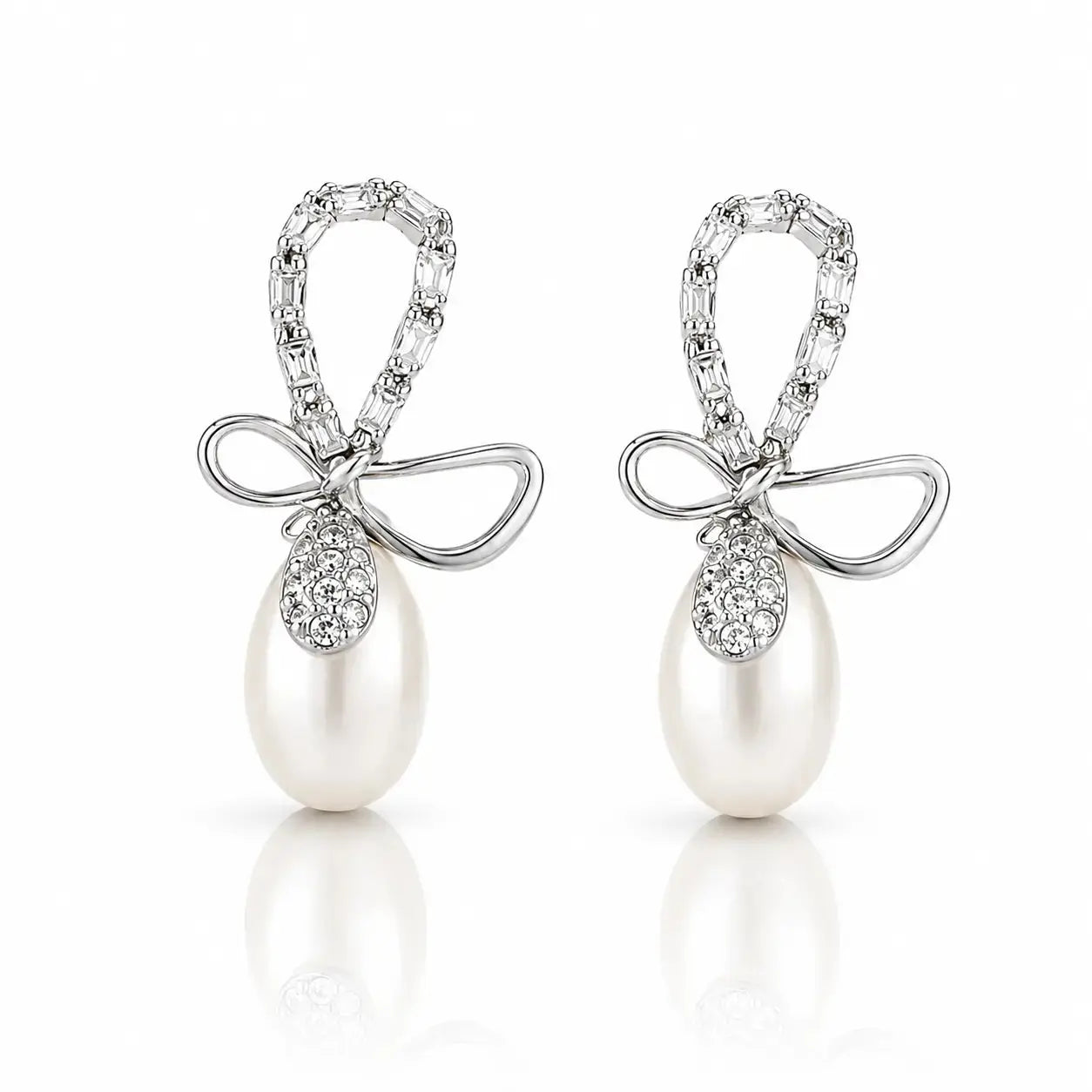 A pair of silver-tone drop earrings featuring a bow-shaped top set with clear pavé stones and a large white pearl dangling below, shown on a clean white background with soft reflections.