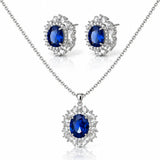 Silver-tone jewelry set featuring a necklace and matching stud earrings with oval deep blue gemstones surrounded by clear crystal halo settings, on a white background.