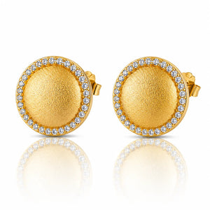A pair of round gold stud earrings with a textured center, a halo border of small clear stones, and post backs, displayed on a reflective white surface.