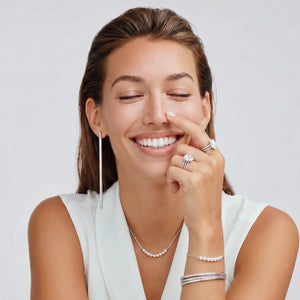 Woman wearing jewelry including earrings, a necklace, ring, and bracelet on a white background