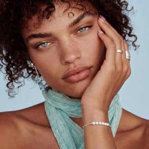 Woman with curly hair wearing a turquoise scarf, earrings, and rings against a light blue background