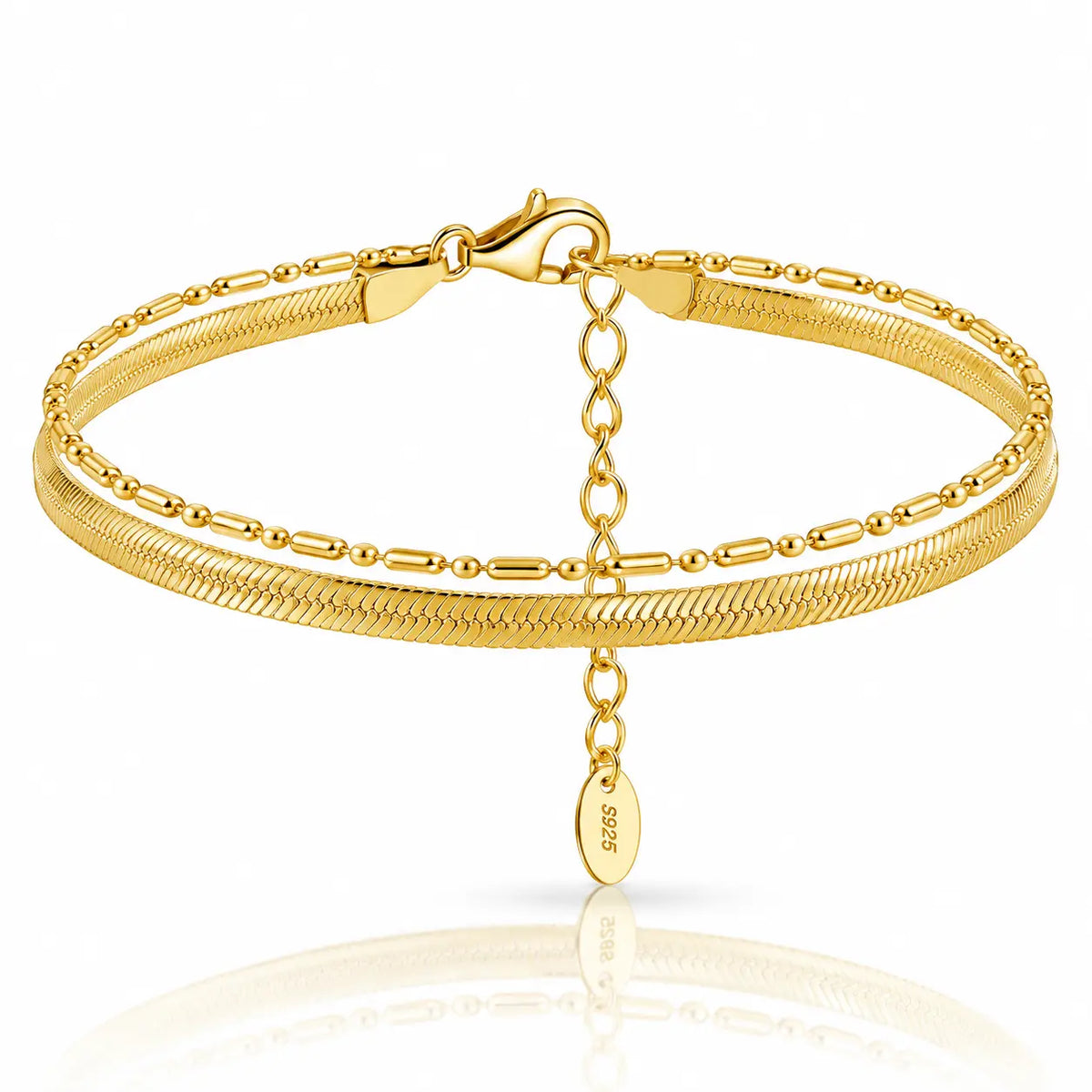 A double-strand gold bracelet featuring a textured snake chain and a smoother tubular chain, with an extender chain and a small oval 925 sterling silver tag hanging from the clasp, set against a white background with a soft reflection.