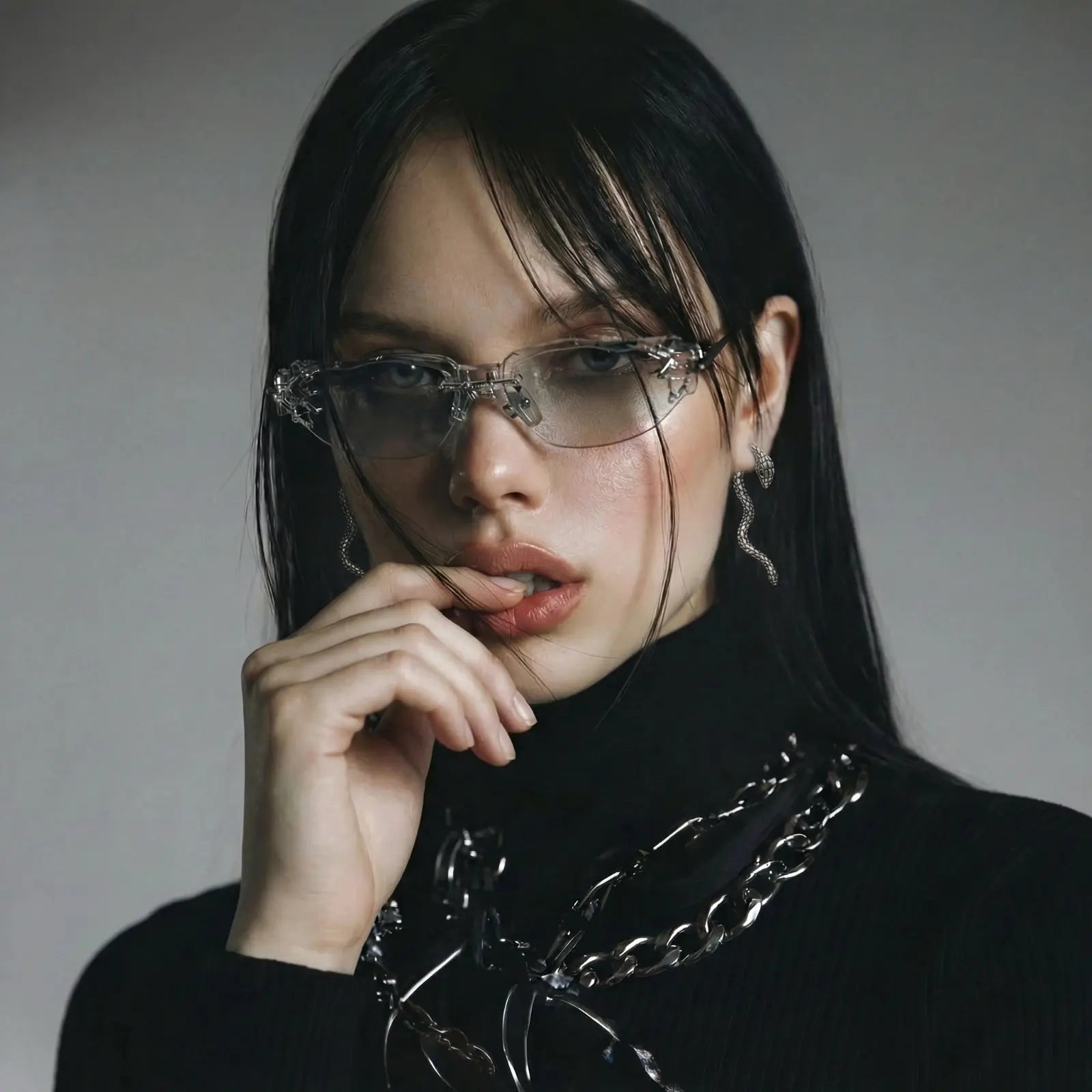 Person wearing glasses and a black outfit with a chain detail on a gray background