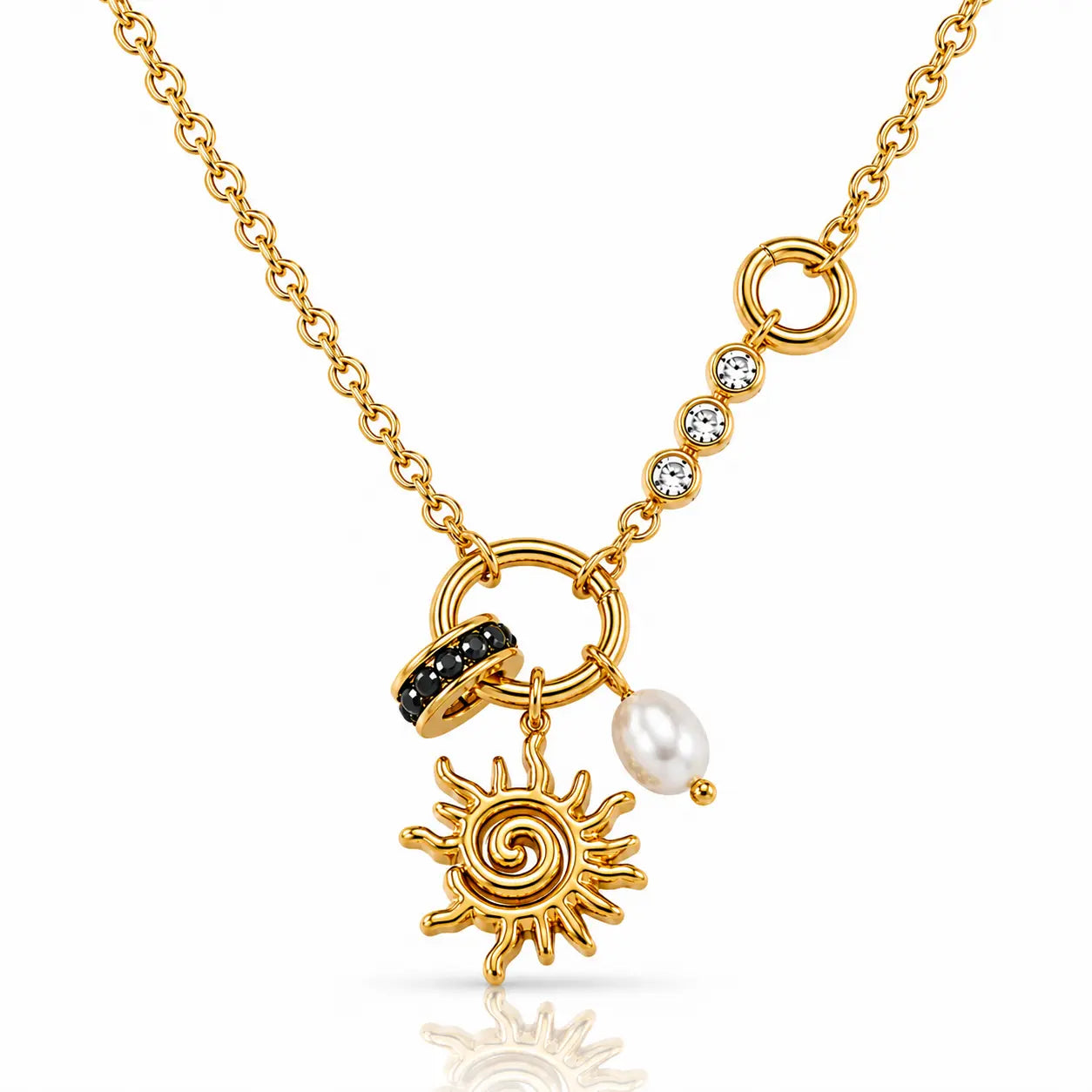 A gold chain necklace featuring a sunburst charm, a black stone-accented ring, a white pearl bead, and a line of clear cubic zirconia stones on a white background.