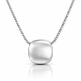 A silver pendant necklace featuring a brushed, rounded square pendant suspended from a delicate silver chain, set against a clean white background with a soft reflection below.