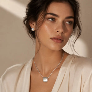 Woman wearing a silver necklace and pearl earring against a neutral background