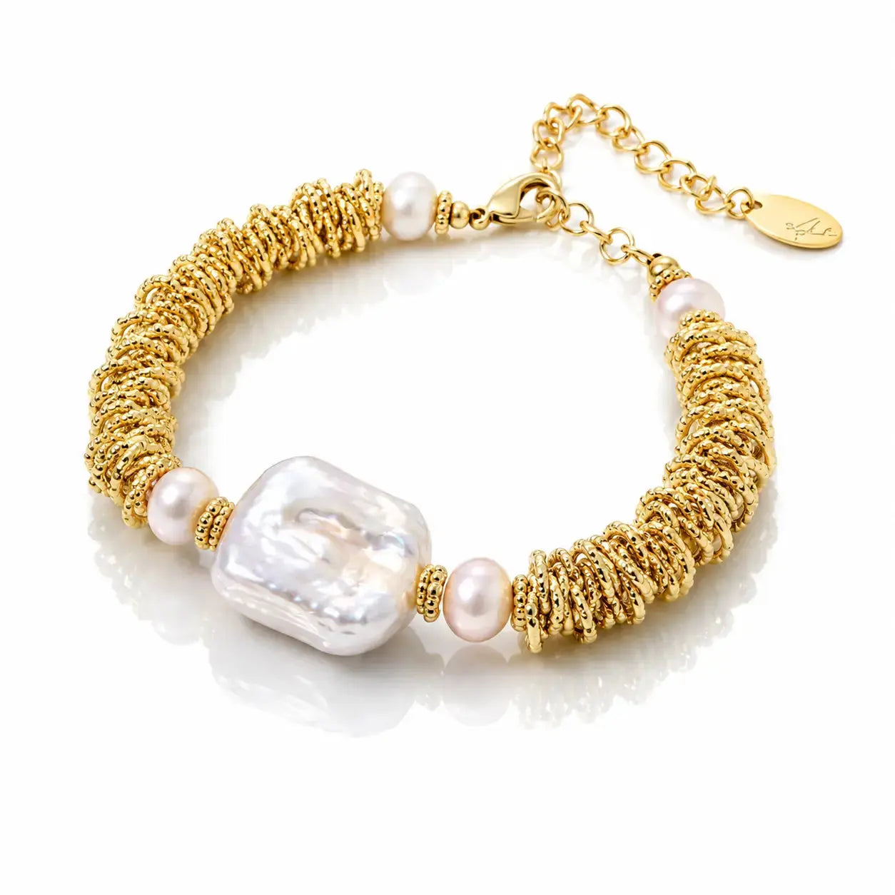 A gold chain bracelet featuring a textured gold rope section, a large baroque pearl, and small pinkish-white pearls, displayed on a reflective white surface.