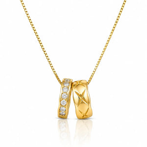 A gold pendant necklace featuring two interlocking bands: one with a row of clear stones and the other with an X-shaped cutout pattern, suspended on a gold chain against a white background.