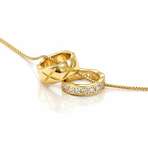 Two gold rings on a gold chain against a white background. One ring features a geometric star pattern, and the other is a smooth band set with small clear stones.